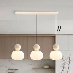 three white lights hanging from the ceiling in a kitchen area with marble counter tops and cabinets