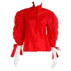 This vintage 1980's Louis Feraud Blouse is in a gorgeous red silk satin and features pretty ruffles and ties. This top has just the right amount of drama with a ruffled collar and red ball buttons down the center front. Each sleeve has three strips of ruffles going from the shoulders to the cuffs, which have pretty ties. This is the kind of blouse that adds depth to a wardrobe and it can be worn with so many separates from jeans to evening skirts! This blouse was originally purchased with a blac Black Ruffled Skirt, Vintage Bodysuit, Edwardian Blouse, Versace Style, Louis Feraud, Evening Skirts, Ruffled Blouse, Bodysuit Blouse, Red Ball