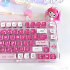 a pink computer keyboard with hello kitty keycaps on the keys and an earphone next to it