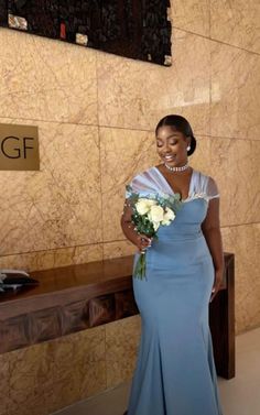 a woman in a blue dress standing next to a wall with flowers and a sign that says gf on it