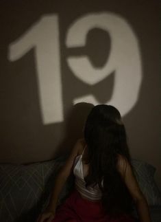 a woman sitting on a bed in front of a wall with the number 19 projected on it