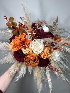 a bridal bouquet with orange, white and burgundy flowers is held by someone's hand