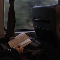 a person sitting on a train holding a book in their hands and looking out the window