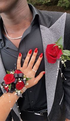 a man and woman are dressed up with red roses on their wrist, holding each other's hands