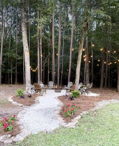 an outdoor seating area surrounded by trees with lights strung from the top and flowers on the ground