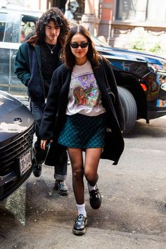 two people walking down the street in front of a car and one is wearing sunglasses