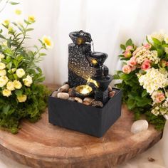 there is a small fountain in the middle of some flowers and rocks on a table