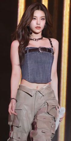 a woman with long dark hair is walking down the runway wearing cargo pants and a denim top