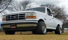 a white pickup truck parked on top of a grass covered field with trees in the background