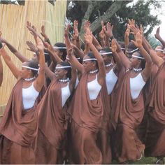 a group of women dressed in brown and white are dancing with their hands up to the sky