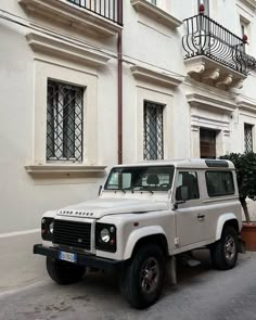 a white land rover is parked in front of a building with balconies on the windows