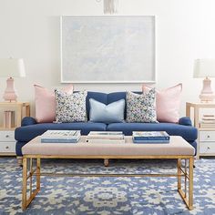 a living room with blue couches and pink pillows on the coffee table in front of it