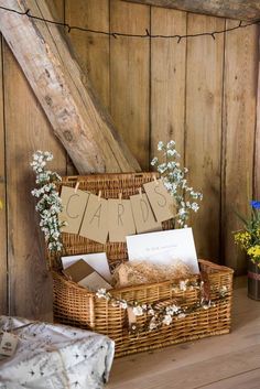 a wicker basket filled with cards and flowers on top of a wooden floor next to a wall