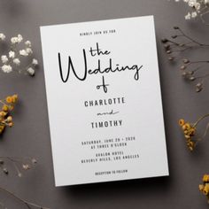 the wedding card is surrounded by flowers and greenery on a gray surface with white paper