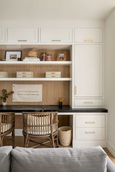 a living room filled with furniture next to a wooden wall mounted book shelf and white cabinets