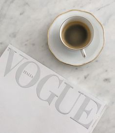 a cup of coffee sitting on top of a white table next to a magazine cover