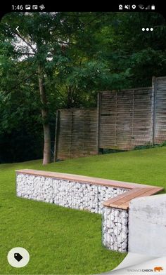 a stone bench sitting in the middle of a lush green field next to a wooden fence