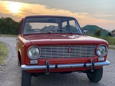 an old red car sitting on the side of a road