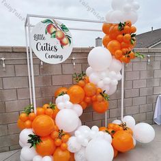 oranges and white balloons are arranged in the shape of a letter made out of fruit