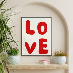 a red love print on a white wall above a shelf with potted plants and books