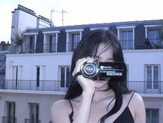 a woman holding a camera up to her face while standing in front of a building