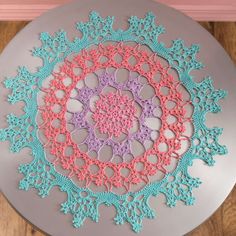 a circular doily with pink and blue crocheted designs on the top, sitting on a table