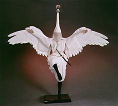 a white bird with its wings spread out on a black stand and it's head turned to the side