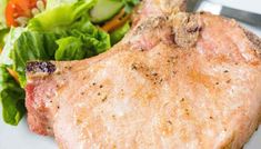 a piece of meat on a plate with a salad and fork in the foreground