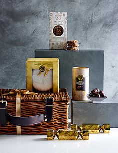 a wicker basket filled with assorted chocolates next to two boxes of cookies