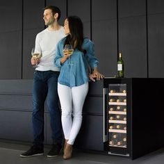 a man and woman standing next to each other with wine glasses in front of them