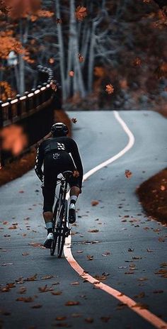 a bicyclist riding down a road in the fall with leaves on the ground