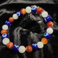 This stylish Mystic 'Merica bracelet features a unique combination of Quartz, Banded Carnelian, and evil eye beads in a patriotic red, white, and blue stretch design. Perfect for anyone looking for a touch of protection and style all in one accessory. White Spiritual Evil Eye Bracelet With Colorful Beads, Spiritual White Beaded Bracelets With Evil Eye, Spiritual White Evil Eye Bracelet With Colorful Beads, Handmade White Evil Eye Spiritual Bracelet, Spiritual White Evil Eye Bracelets, Handmade White Spiritual Evil Eye Bracelet, Symbolic White Round Bead Bracelets, Symbolic White Bracelets With Round Beads, White Evil Eye Bracelet With 8mm Beads As Gift