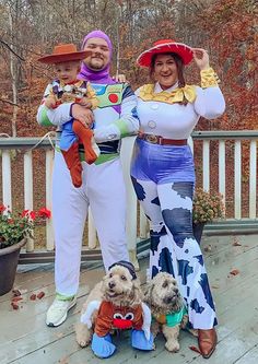 two people in costumes standing on a porch with their dogs and one is holding a toy