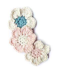 three crocheted flower appliques are shown on a white surface, one is blue and the other is pink