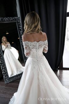 a woman in a white wedding dress looking at herself in the mirror with her reflection