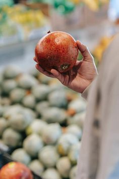 a person holding an apple in their hand near other fruit at the produce section of a grocery store