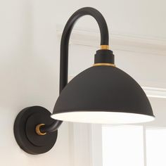 a black and gold wall light with a white shade on the top, in a room