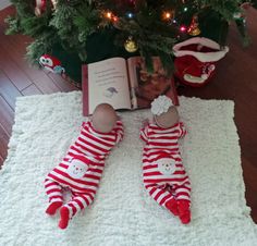 two babies are laying on the floor next to a christmas tree and an open book