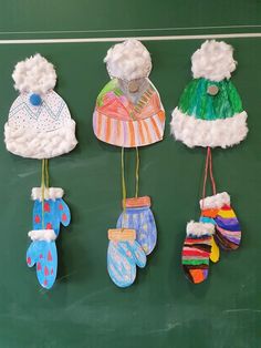 four handmade hats and mittens hanging from strings on a green board with white writing