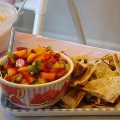 a bowl of fruit salsa with tortilla chips on a tray next to a container of dip