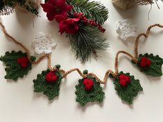 crocheted holly ornaments hanging from twine with red flowers and green leaves on them