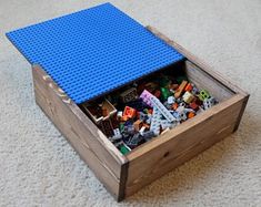 a wooden box filled with legos on top of a white carpeted floor next to a blue lid