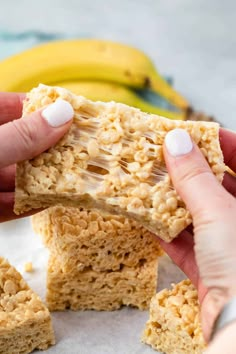 someone is holding some rice krispy treats in front of two bunches of bananas