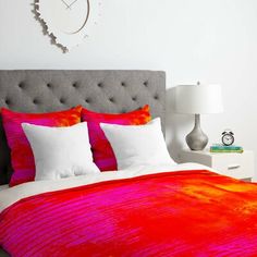 a bed with red and orange comforter in a bedroom next to a white wall