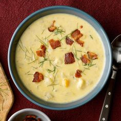 there is a bowl of soup with bacon and cheese in it next to a spoon