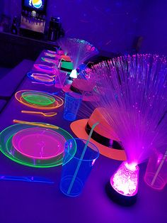 a long table is lit up with neon colored plates and vases on top of it