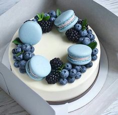 a cake decorated with macaroons, blueberries and blackberries in a box