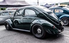 an old green car parked in a parking lot next to other antique cars on display