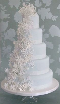 a three tiered cake with snowflakes on the top is displayed in front of a floral wallpaper