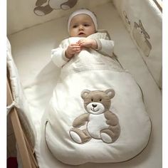 a baby laying in a crib with a teddy bear blanket on it's side